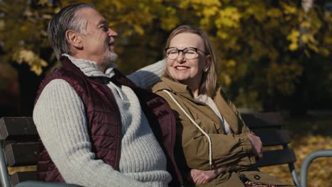 caucasian senior couple sitting at the bench at park and embracing