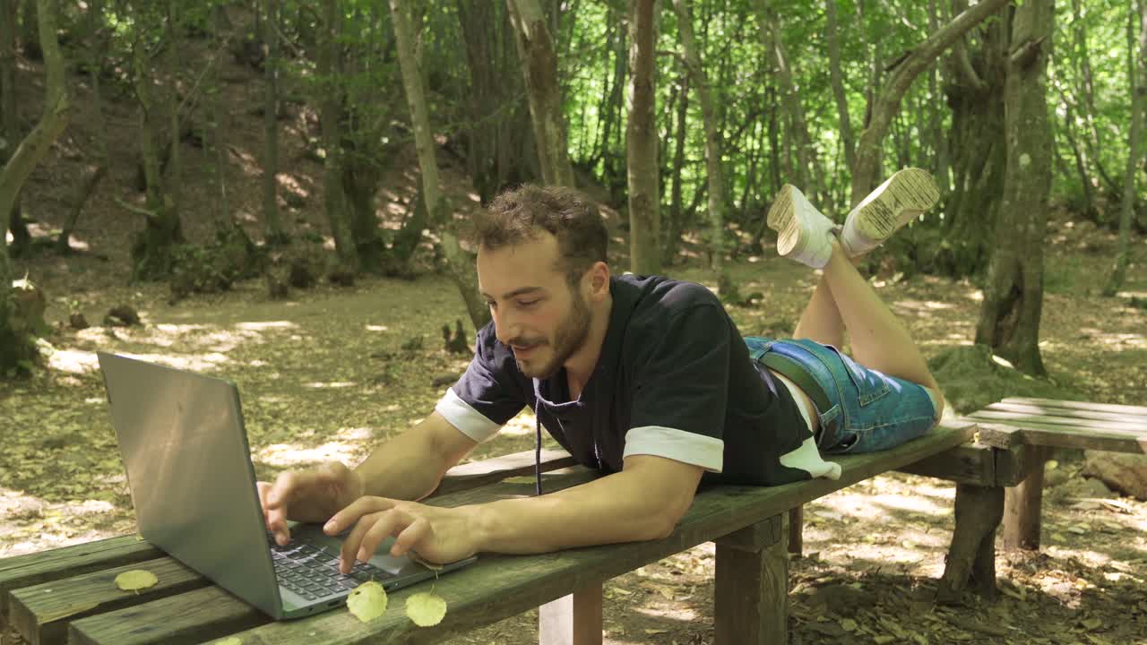 Young man working with laptop in forest.