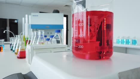 middle shot of a magnetic stirrer stirring a red transparent liquid in a beaker glass and some other lab bottles and equipment static shot