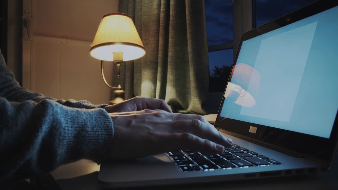 Typing adult hands in sweater at home working late, landing on keys, pressing laptop, lamp glowing