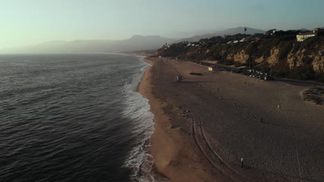 Una-Foto-De-Ariel-De-Una-Playa-Cerca-Del-Acantilado-De-Point-Dume-En-Malibu-En-California-Mientras-Las-Olas-Ruedan-Sobre-La-Arena-En-La-Noche-Mientras-Las-Puestas-De-Sol