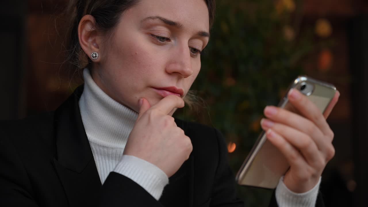 Close up of a brunette woman in a white turtleneck scrolling through her phone