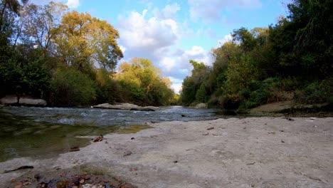 Panning-across-large-rock-towards-a-creek---the-tops-of-trees-illuminated-by-the-sun-setting---beautiful-clouds-in-the-sky