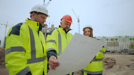 group of builders and engineers are inspecting construction plan of new object in building site