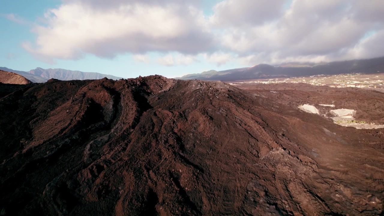 Lava negra fresca estende-se em direção a estufas e telhados espalhados por um amplo vale verdejante.
