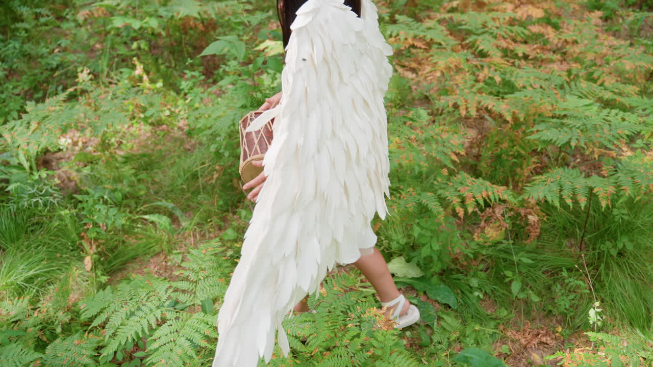 Aerial view of beloved of Eros with graceful angelic wings walking slowly through lush forest, softly beating small kalimba drum, surrounded by ferns and sunlight