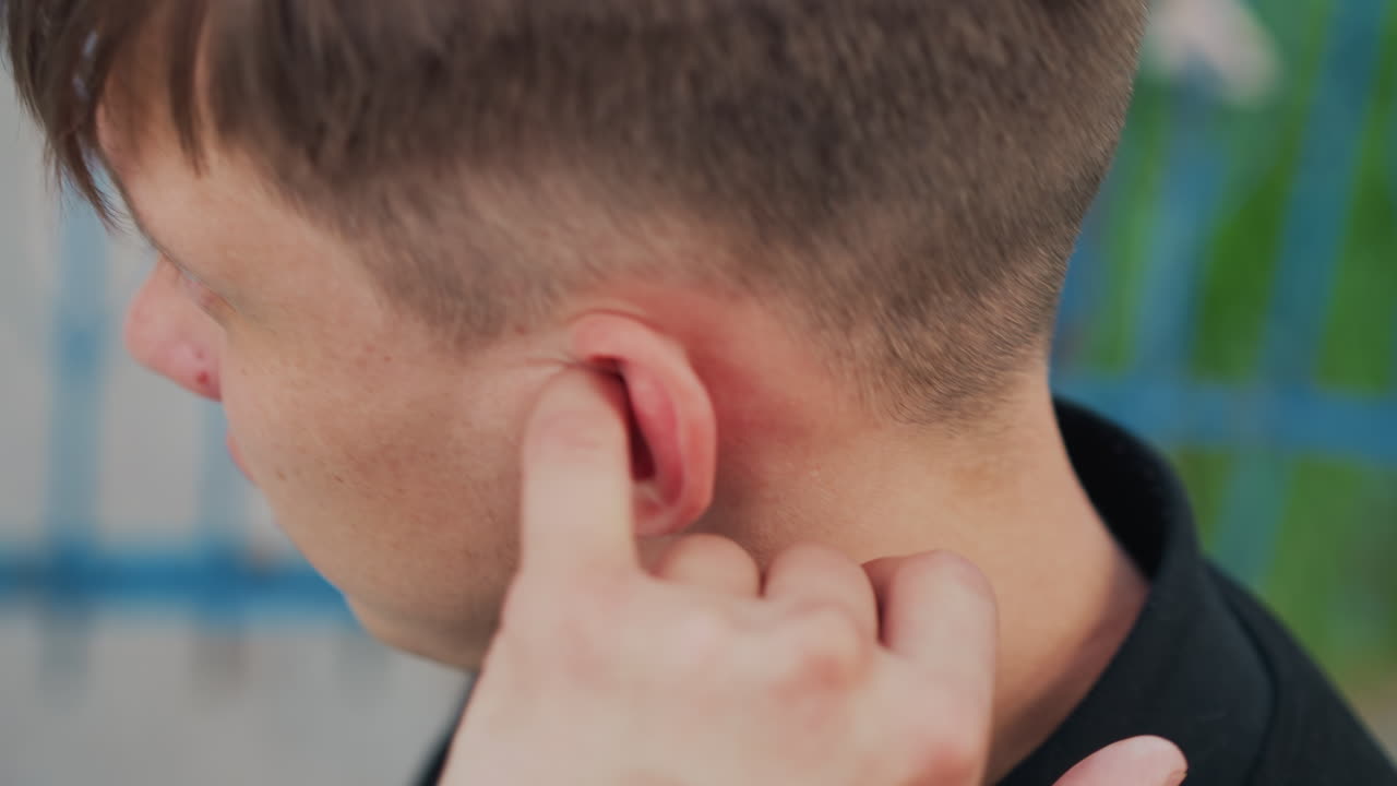 Un adolescente se enjuaga el oído después de nadar al aire libre, vista lateral sincera de un joven aliviando la irritación del agua en el oído, un joven en traje de baño casual aliviando las molestias en el oído después de una sesión de piscina al aire libre