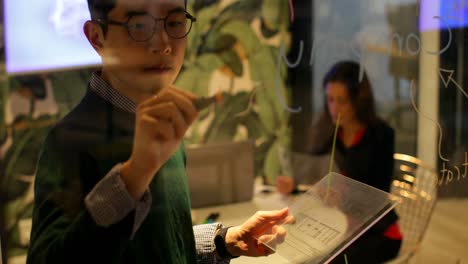 male executive writing on glass board while using digital tablet in office 4k