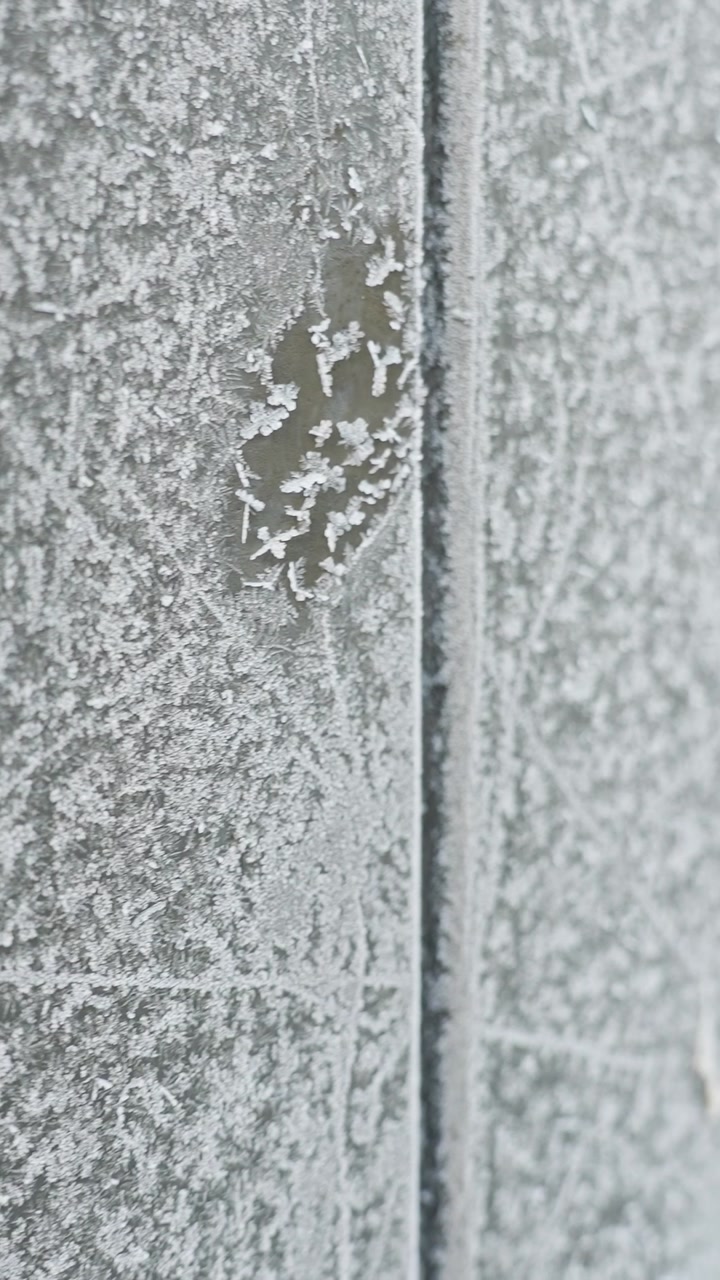 Close-up of frost-covered winter fence with icy crystal texture and rime patterns. Minimal cold background for seasonal design, weather concept, and vertical macro b-roll.