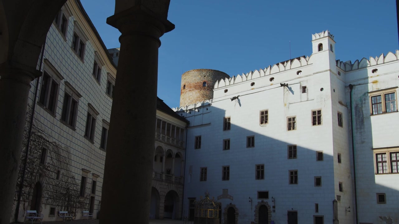 Colonne ad arco che incorniciano il cortile del castello di Jindřichův Hradec con una torre rotonda medievale, Repubblica Ceca, panoramica.