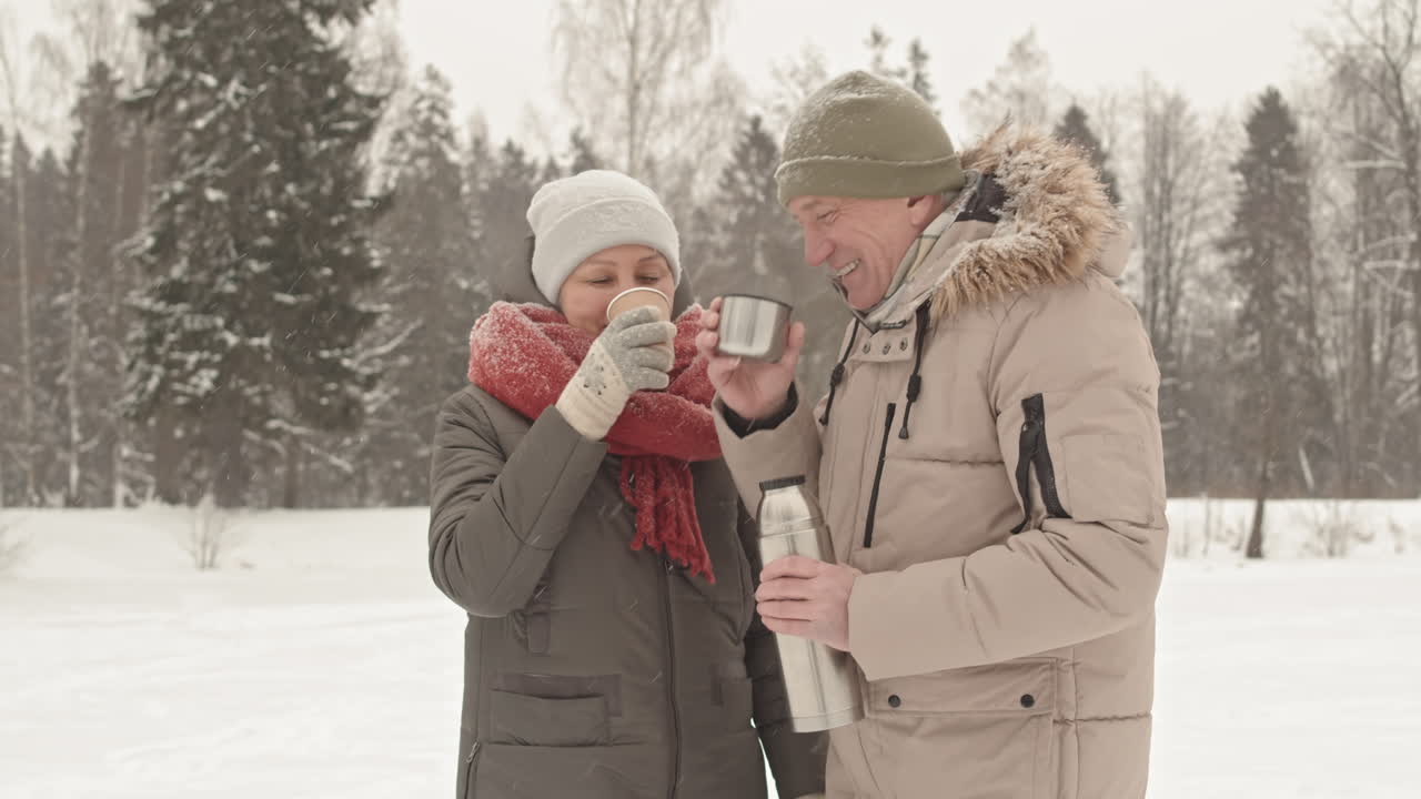 una pareja de ancianos disfrutando de bebidas calientes en un parque nevado