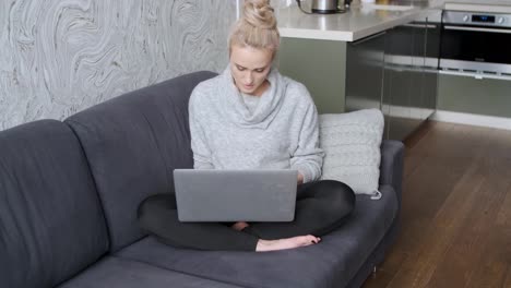 Fröhliche-Junge-Blonde-Frau-Sitzt-Auf-Der-Couch-Im-Wohnzimmer-Und-Benutzt-Laptop