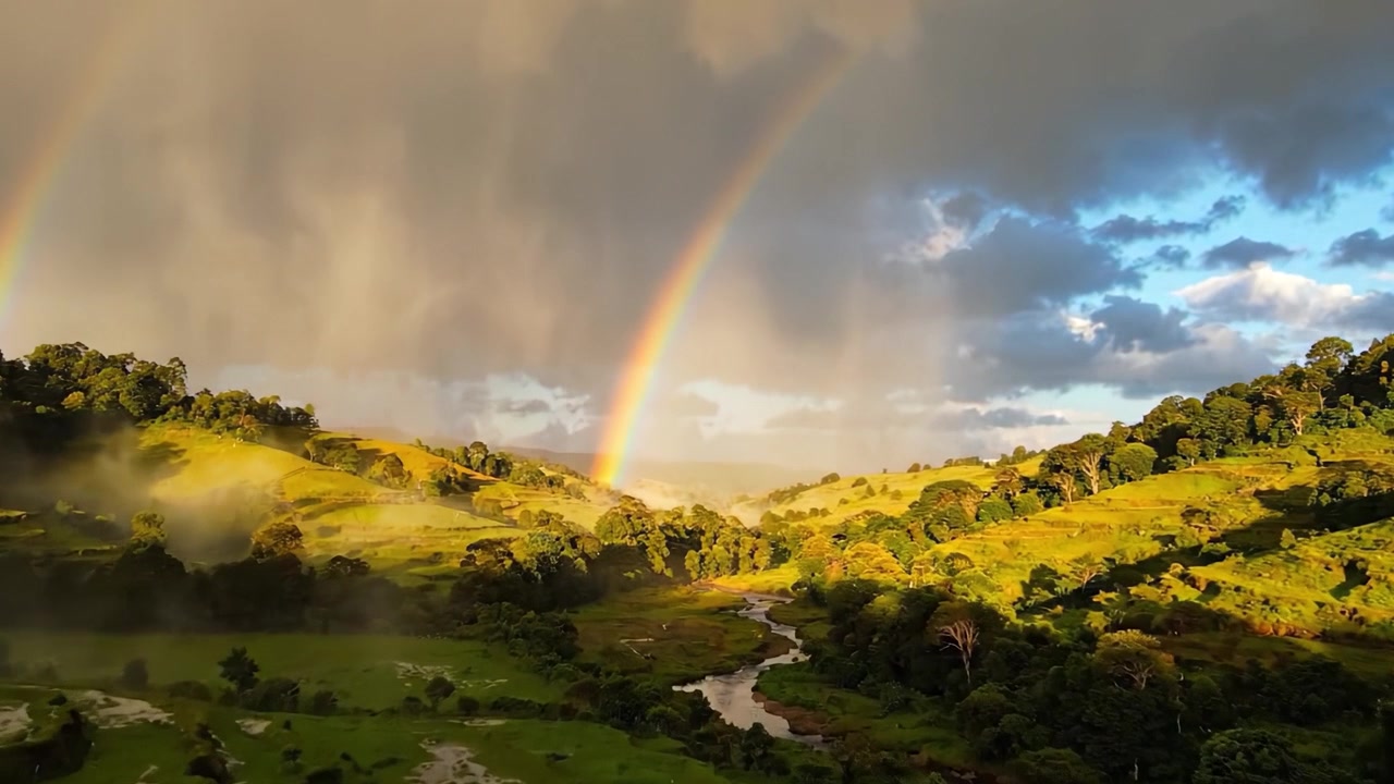 A Stunning View of a Lush Green Valley Underneath a Bright Rainbow with Dramatic Skies and Mist Rolling Over the Landscape