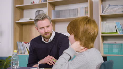 redheaded student sitting at the desk in english classroom while the teacher answers him some questions 2