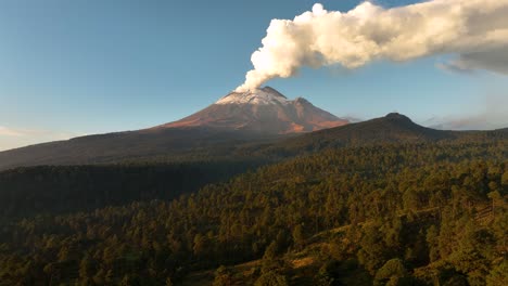high‑altitude drone push‑in glides above vast dawn forest, revealing popocatepetl’s snow‑capped cone and thick fumarole against pastel sky—ideal opener for travel, nature or news projects.