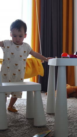 small kid moves the chairs from the table. toddler touches the toys on the desk and then lowers to the floor. vertical video