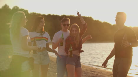 un grupo de estudiantes celebra el final del semestre con cerveza en la playa de arena. están bailando en la fiesta al aire libre al atardecer.