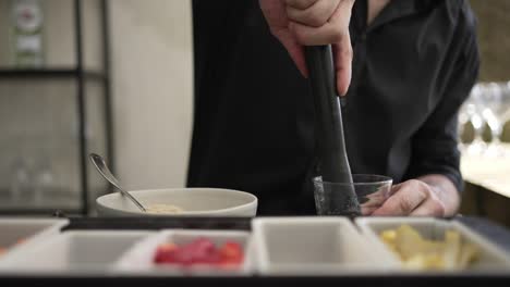 bartender muddling ingredients in a glass with various garnishes on the bar counter