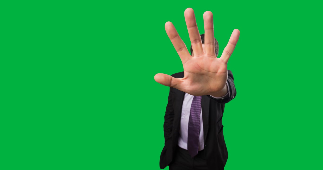 Ritratto di uomo d'affari che fa il segno di stop con la mano su sfondo nero.