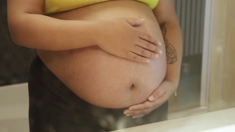 pregnant light skin woman holding her baby belly in the bathroom mirror