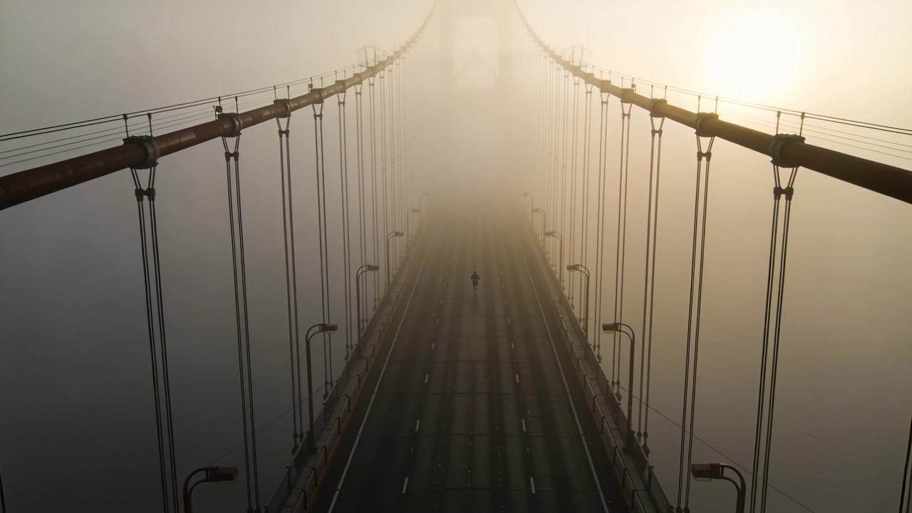 Pedone solitario che cammina verso un arco distante su un ponte nebbioso, con il sole che filtra da destra.