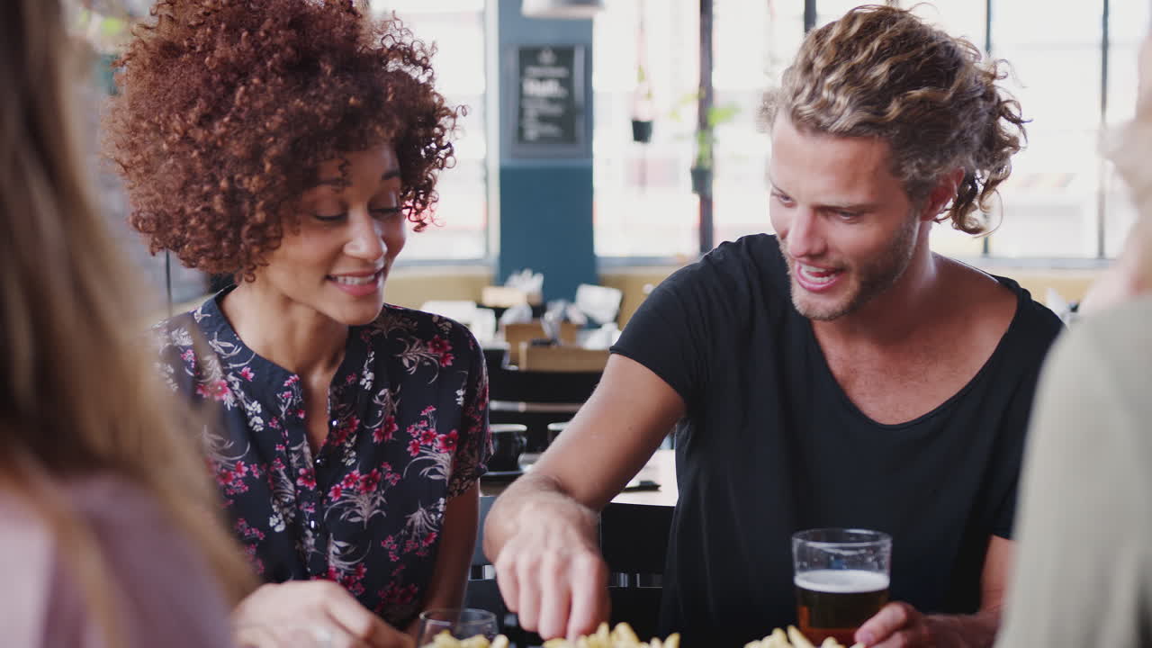 grupo de amigos comiendo papas fritas mientras se reúnen en la barra del restaurante