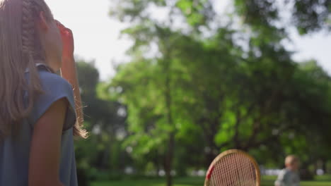 Bored-girl-play-badminton-with-brother-touching-racket-net-in-park.-Rear-view