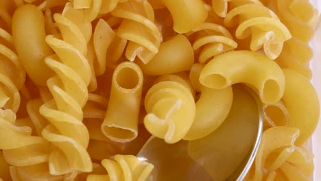 spiral and elbow pasta fall into a shiny spoon, captured in bright, even lighting with a close-up focus