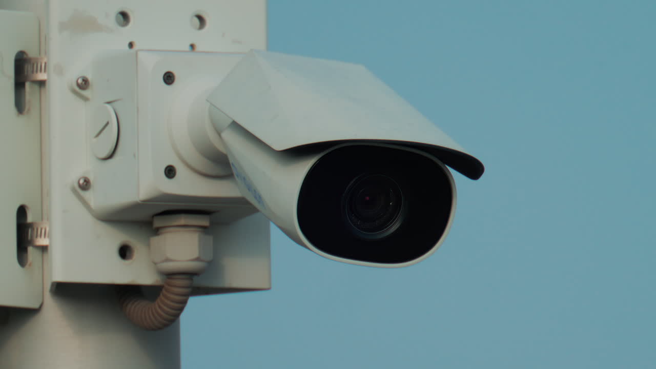 A close up of a modern black surveillance camera turning against a bright sky background