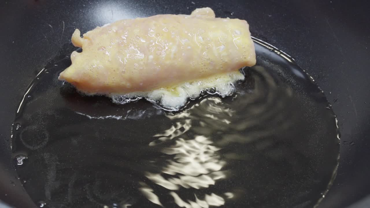 Close-up of stuffed chicken rolls placed in hot oil, beginning to cook in a pan