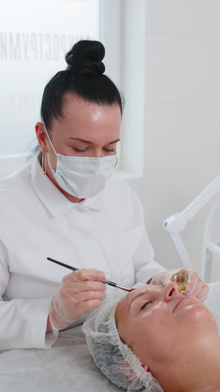 terapia enzimática esteticista aplicando crema médica hidratante en la cara de una mujer joven adulta con pinceles