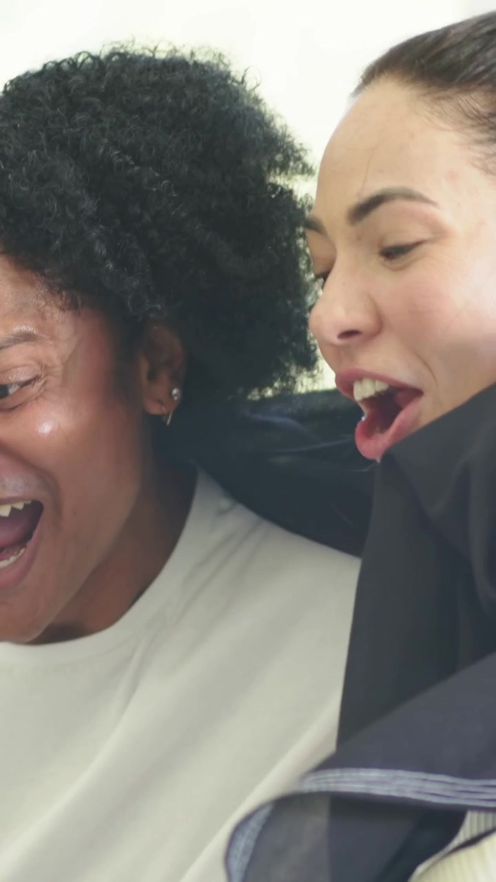Vertical video: Laughing two women reacting after surprise offscreen in bright room, red jacket
