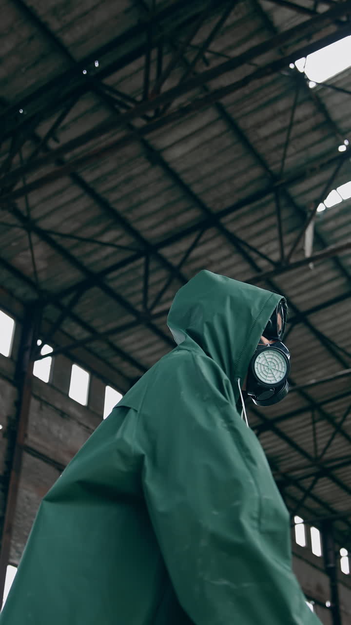 Human in a respirator and a hood is standing in abandoned building. Survivor on the background of a ruined building with holes on roof. Vertical video