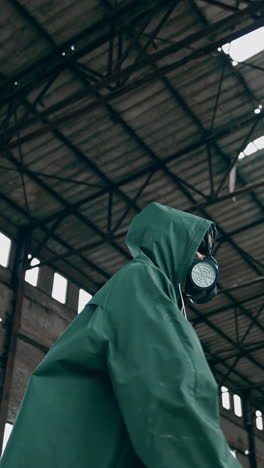 human in a respirator and a hood is standing in abandoned building. survivor on the background of a ruined building with holes on roof. vertical video