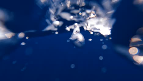 Jumping-into-deep-blue-ocean-water-and-swimming-through-choppy-swell,-waves-and-bubbles-in-vast,-remote-sea