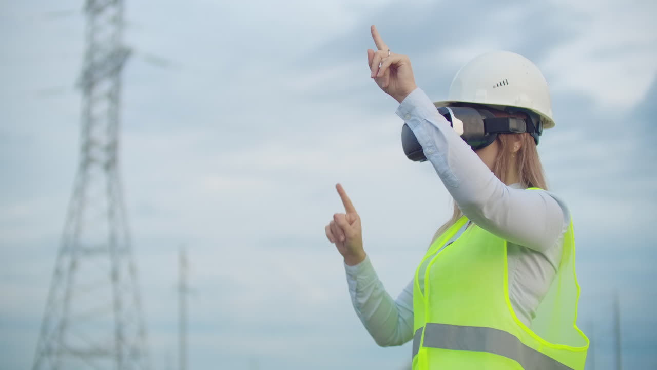una mujer electricista con gafas de realidad virtual mueve su mano simulando el trabajo con la interfaz gráfica de una central eléctrica contra el fondo de líneas de transmisión eléctrica de alto voltaje.