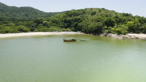 Drone-approaching-a-small-boat-in-a-Jungle-Beach-on-tropical-coast-brazilian-ocean,-Zimbros,-Brazil