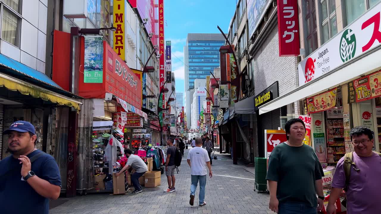 A lively Japanese city street with people walking past colorful shops and billboards on a sunny day