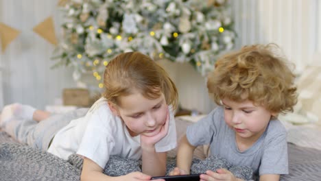 Junge-Und-Ein-Mädchen-Liegen-Auf-Einer-Decke-Und-Schauen-Zu-Weihnachten-Auf-Das-Handy