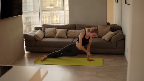 mujer haciendo ejercicio en casa practicando varias asanas de yoga, haciendo una postura de perro hacia abajo en la sala de estar en una alfombra de entrenamiento amarilla. cámara lenta