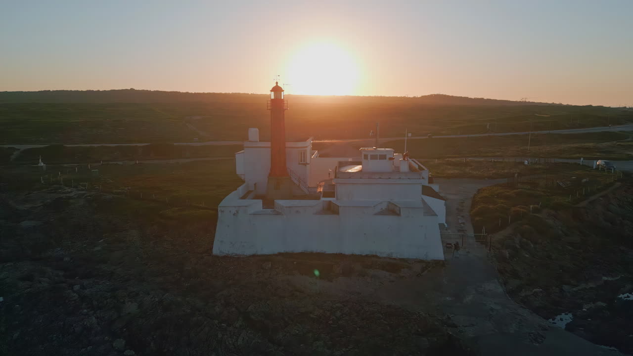 Luce brillante del tramonto che illumina un alto faro costiero, vista aerea. Faro rosso.