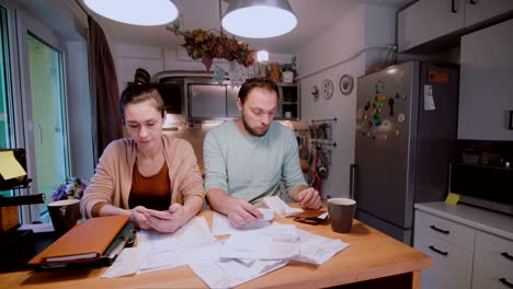 un hombre y una mujer sentados en la cocina clasificando cheques y cuentas.