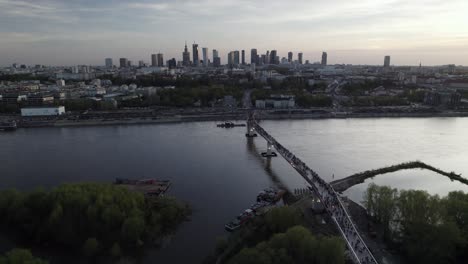 Dusk-glow-spreads-over-Vistula-river-as-crowds-of-people-cross-bridge-entering-Warsaw-Poland