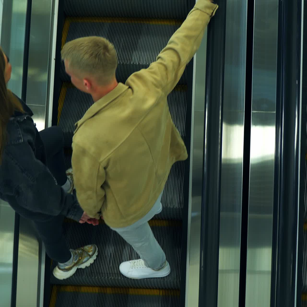 Metal escalator stairs moving in both directions up and down. Young couple standing on the steps, embracing and going up. Top view