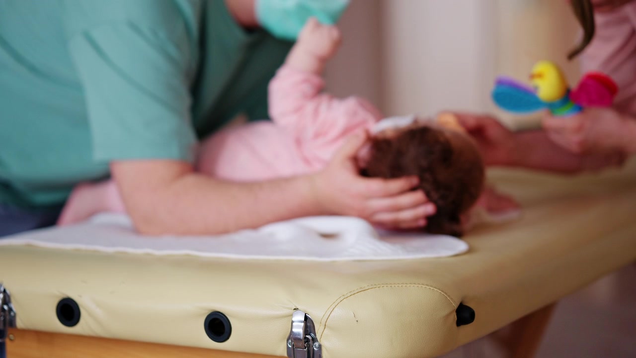 Neonato che riceve un delicato supporto da adulti su un lettino da trattamento, mentre un giocattolo colorato viene usato per coinvolgerlo