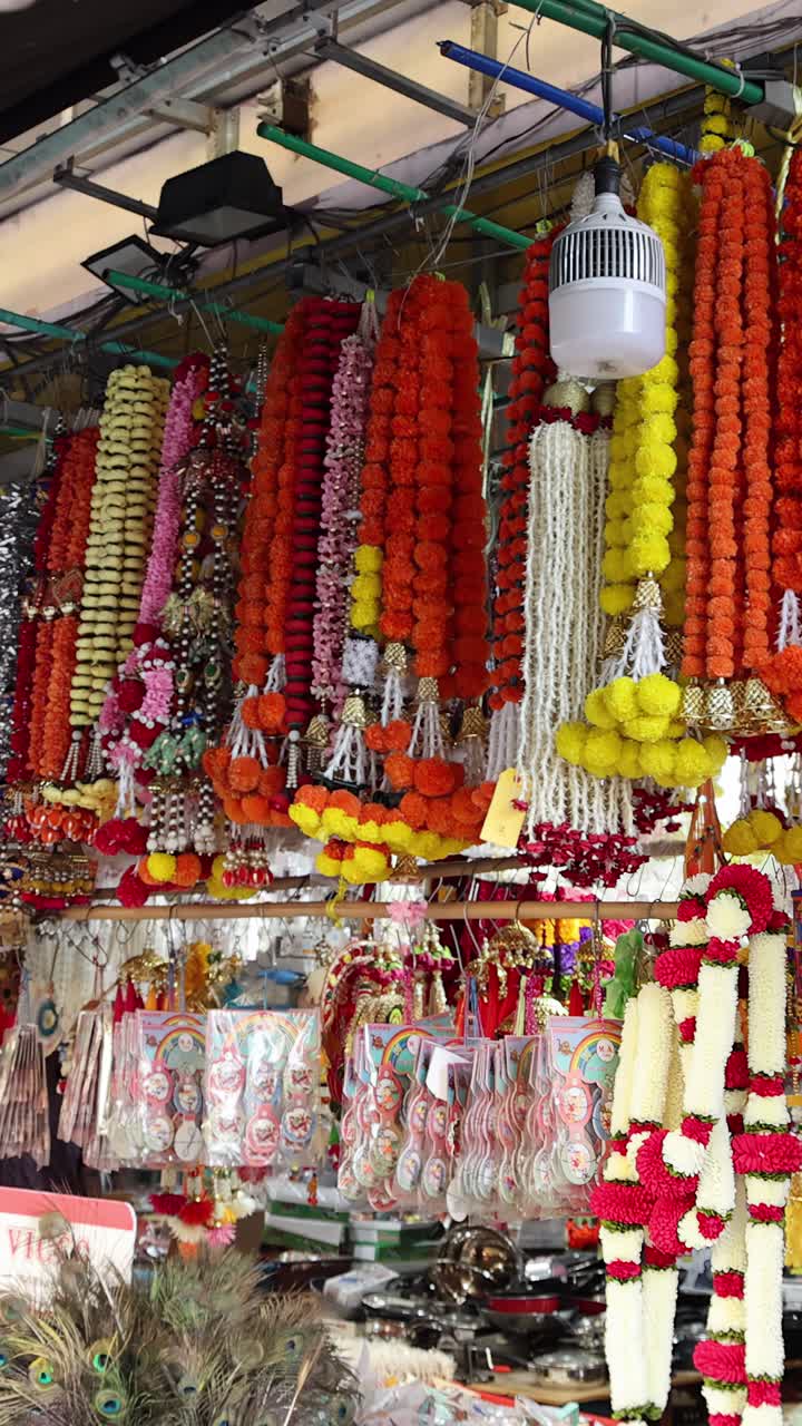 A vibrant flower garland shop in an outdoor market, filled with marigold and jasmine garlands, as the camera slowly pulls back to reveal a customer