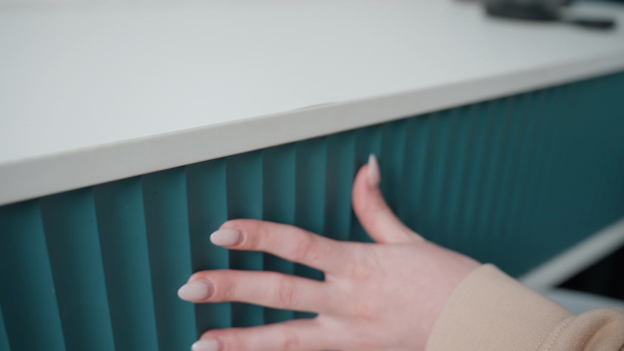 Nærbillede af turkis skuffe, hånd åbner, hjemmeunderviser arrangerer studiematerialer, langsom taktil bevægelse, hvidt minimalistisk skrivebord, ribbet tekstureret panel, neutral manicure på fingre, blødt naturligt lys, stille fokuseret.