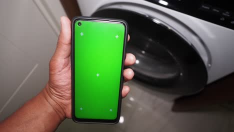 hand holding a phone with a green screen in front of a washing machine
