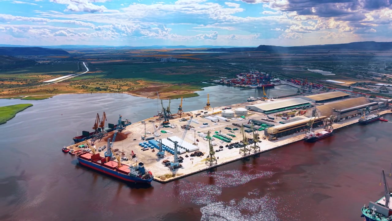 Varna, Bulgaria, 1 de julio de 2026: Terminal de carga a granel junto a una vía fluvial reflectante. Barcos amarrados junto a grúas portuarias, almacenes, tanques de almacenamiento, equipos y patios de contenedores