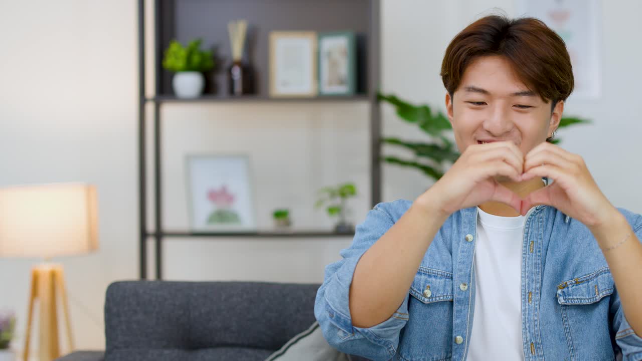 陽気な若いアジア人男性が、カメラに向かって笑顔でハートのジェスチャーをしています。